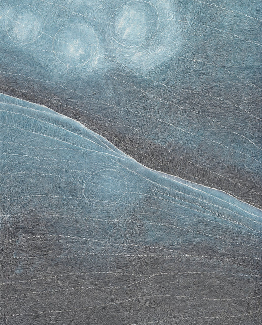 Large dot painting in slate blue, charcoal and silver, divided by a sweeping diagonal ridge, with luminous pale circles hovering in the upper sky-like field and dense layered dotwork suggesting an aerial view of Country.